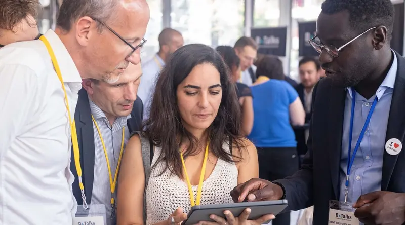 B.Talks 2024 : une participante tient la tablette de l’escape game, entourée de trois commerciaux et partenaires penchés sur l’écran