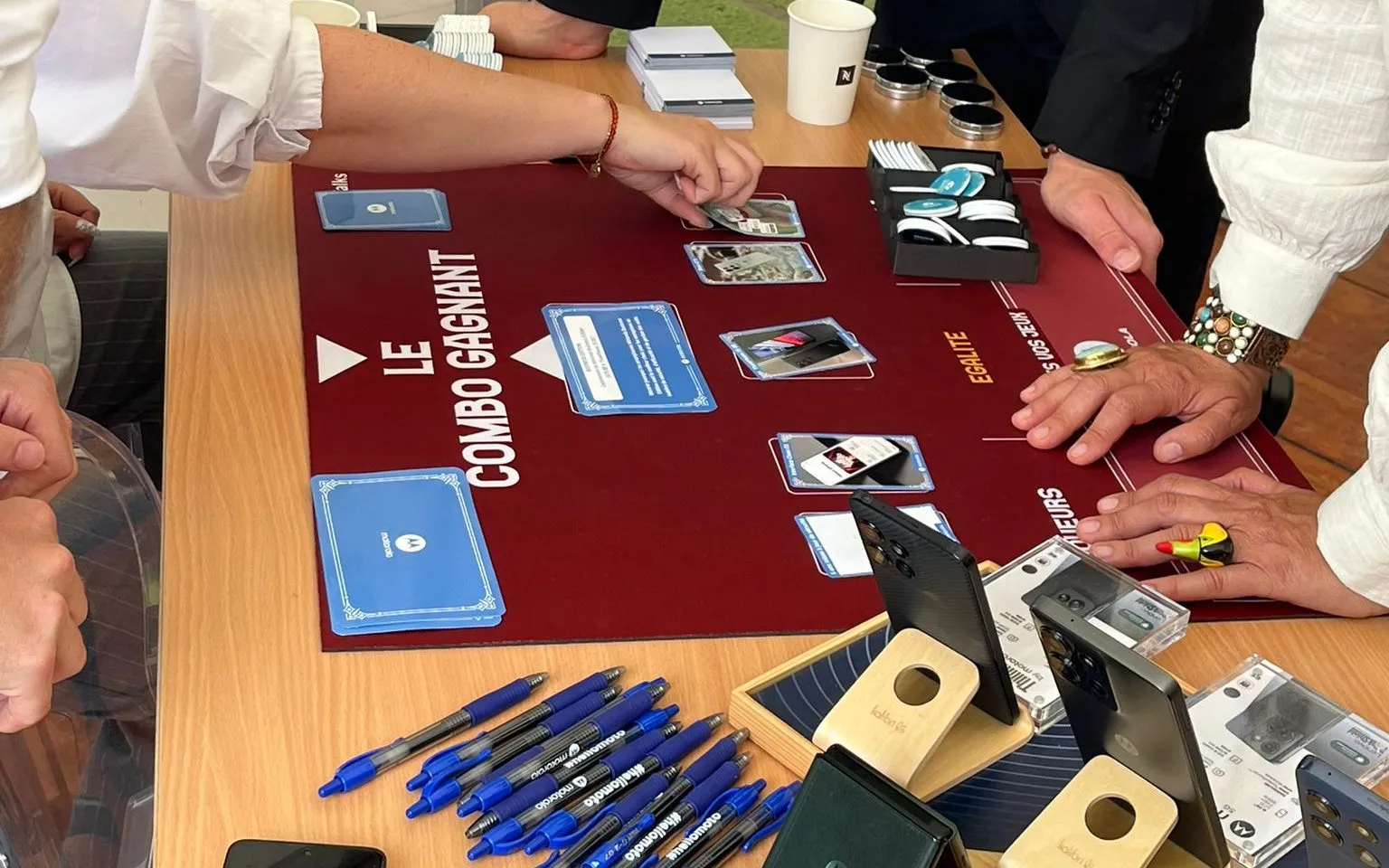 B.Talks 2025 : table Motorola du Grand Casino, un participant pose une carte sur le tapis bordeaux « Le Combo gagnant », à côté des smartphones du partenaire