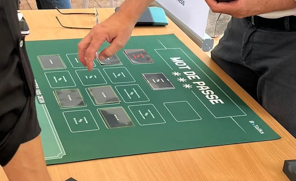 Mise en situation sur un plateau de jeu à tapis vert : un participant pose une carte sur la grille pendant que les autres observent