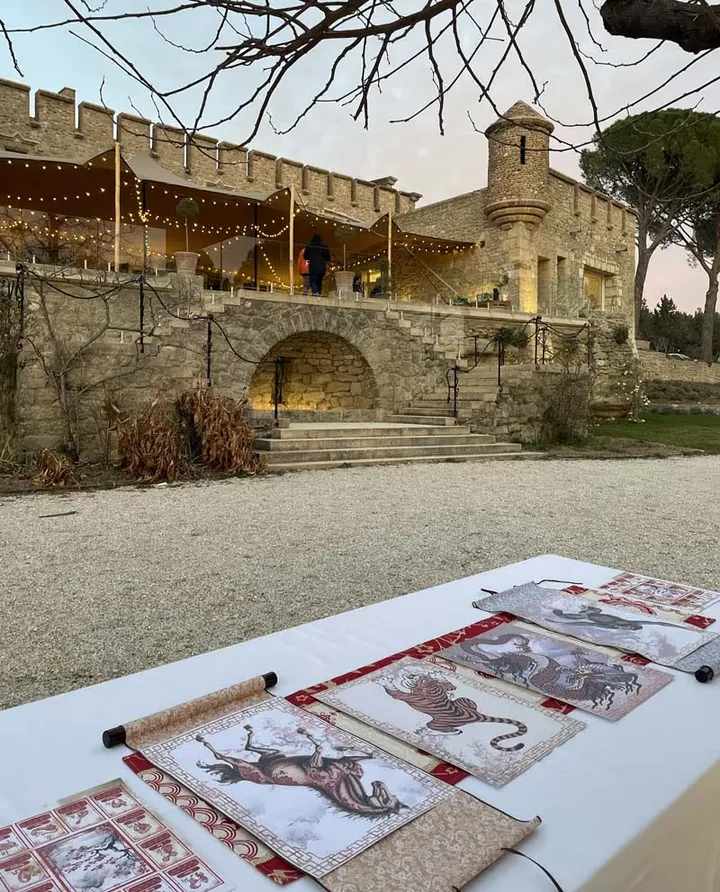 Cour d’un château illuminé : rouleaux illustrés d’un tigre, d’un cheval et d’un dragon déroulés sur une table au premier plan