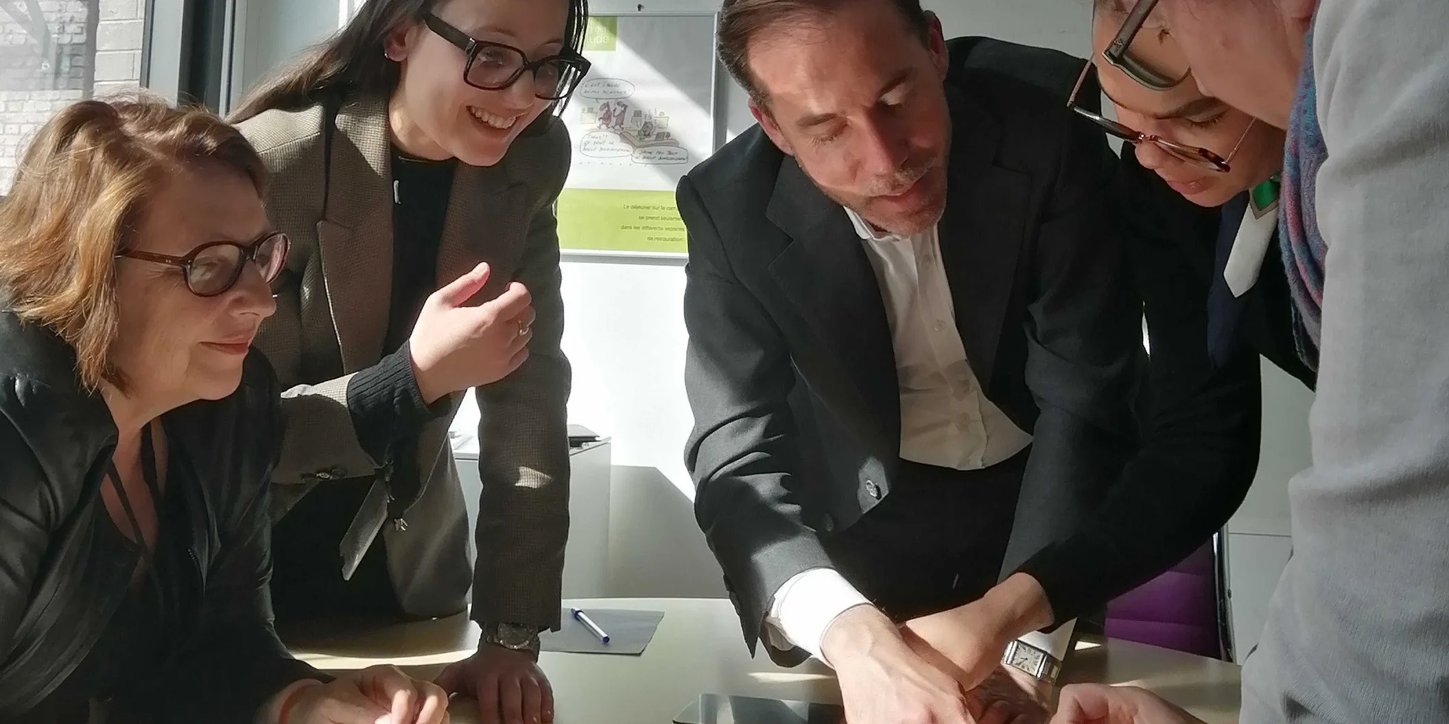 Crédit Agricole : cinq collaborateurs penchés sur la table pendant une session de l'escape game, deux d'entre eux manipulent ensemble un élément du jeu