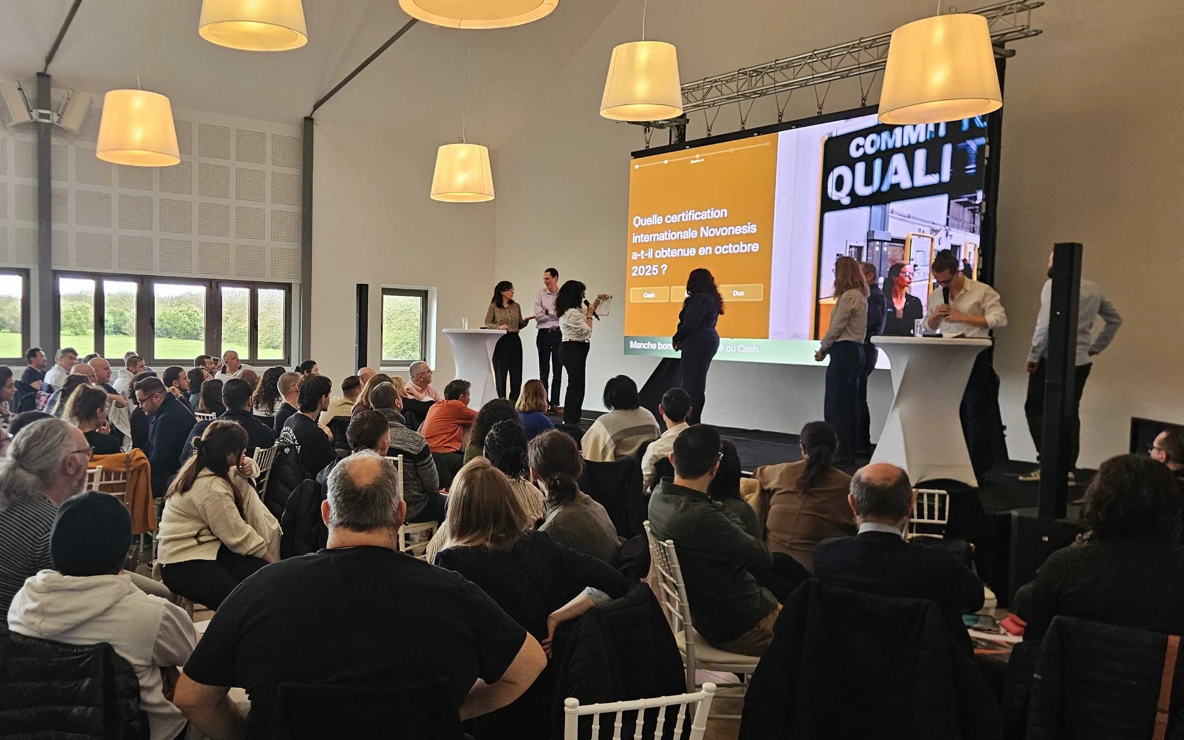 Novonesis : plénière au Domaine du Palladium, le grand écran affiche une question du quiz sur la certification obtenue en octobre 2025, des participants sont sur scène et le public est vu de dos