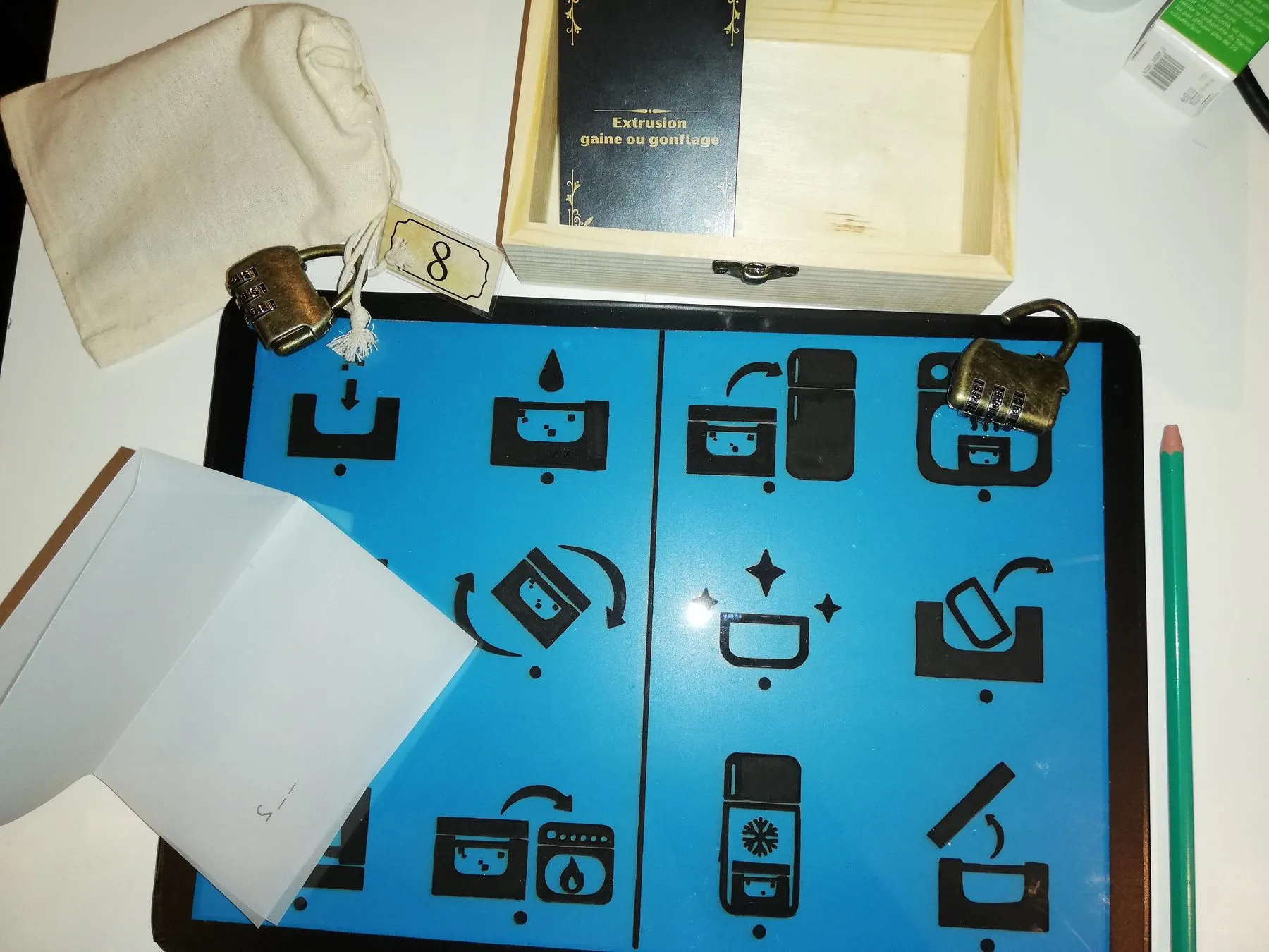 « Le secret d'Eugène », version en salle : plateau d'énigmes bleu à pictogrammes, cadenas à code et coffret en bois pendant un test du jeu
