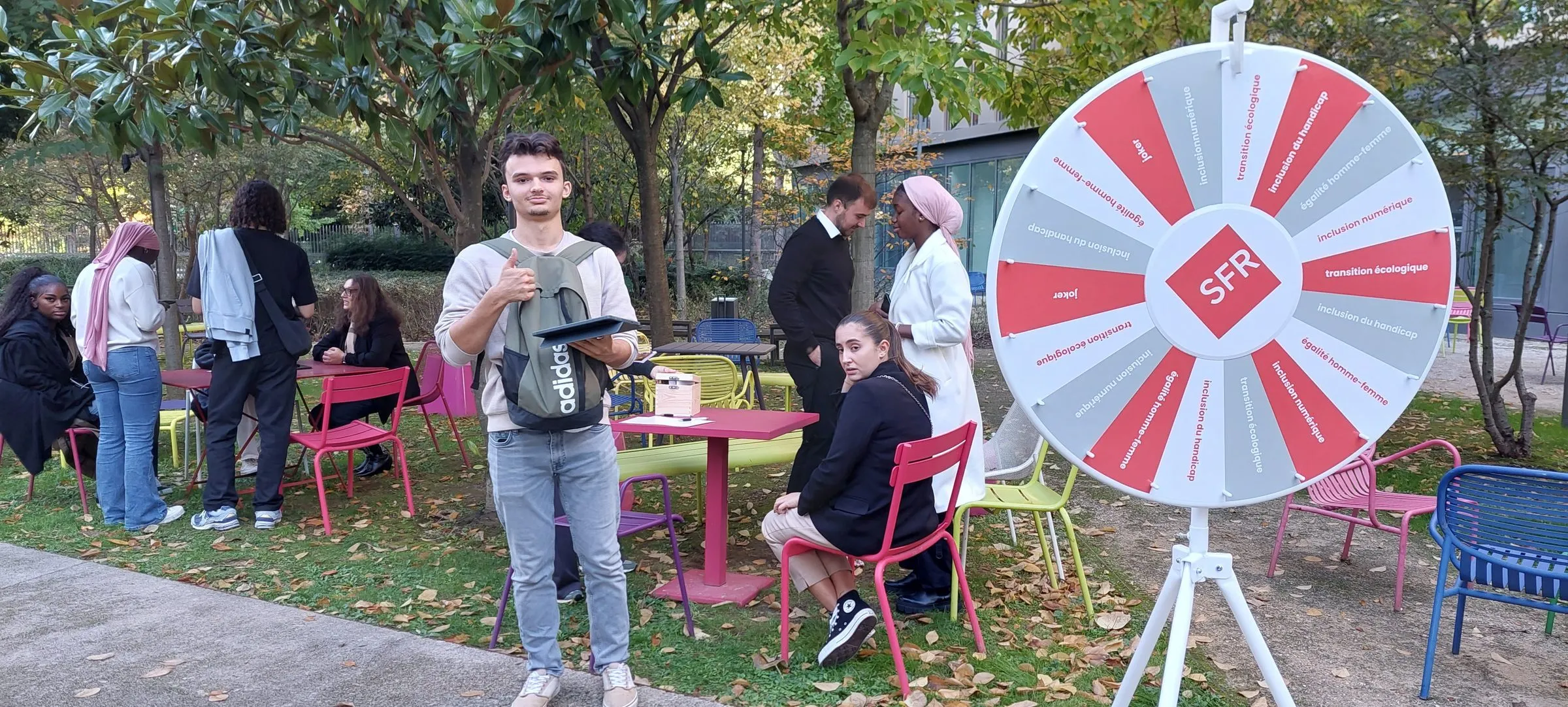 SFR : dans le jardin du campus, un alternant tablette en main devant la roue de l’engagement aux couleurs de SFR