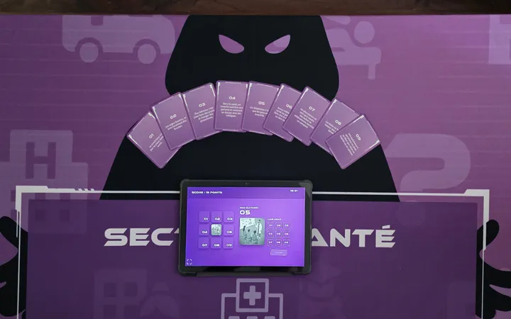 Béthune-Bruay : tapis de jeu « Secteur santé » vu du dessus, avec la silhouette encapuchonnée, l’éventail de cartes numérotées et la tablette du jeu